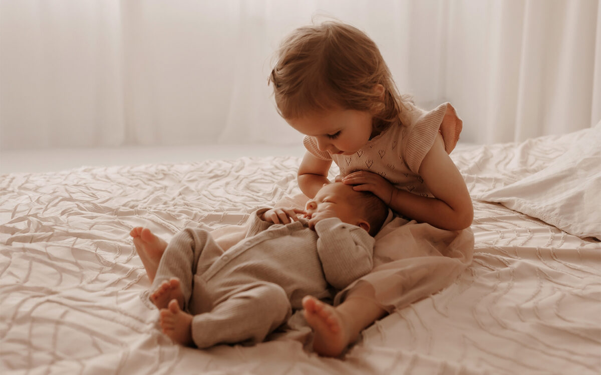 Geschwisterfoto aus einem Babyshooting in München: Kleinkind liegt liebevoll neben seinem neugeborenen Geschwisterchen in warmen Naturtönen.